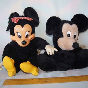May include: A black and brown plush Mickey Mouse and Minnie Mouse toy set. Minnie Mouse is wearing a red and white polka dot bow.