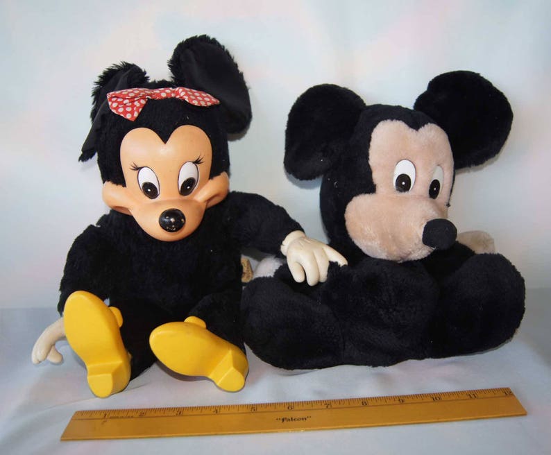May include: A black and brown plush Mickey Mouse and Minnie Mouse toy set. Minnie Mouse is wearing a red and white polka dot bow.