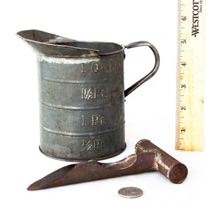 May include: A vintage metal measuring cup with a handle, marked with measurements in quarts and pints. A rusty metal tool with a handle is also pictured.