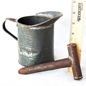 May include: A vintage metal measuring cup with a handle and a rusty metal tool with a T-shaped handle. The measuring cup is marked "1 Qt. Liquid".