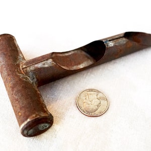 May include: A rusty metal tool with a T-shaped handle and a long, curved, hollow tube. The tool is about the size of a quarter.