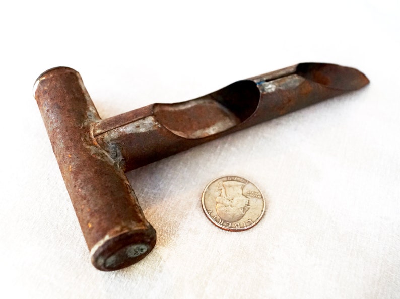 May include: A rusty metal tool with a T-shaped handle and a long, curved, hollow tube. The tool is about the size of a quarter.