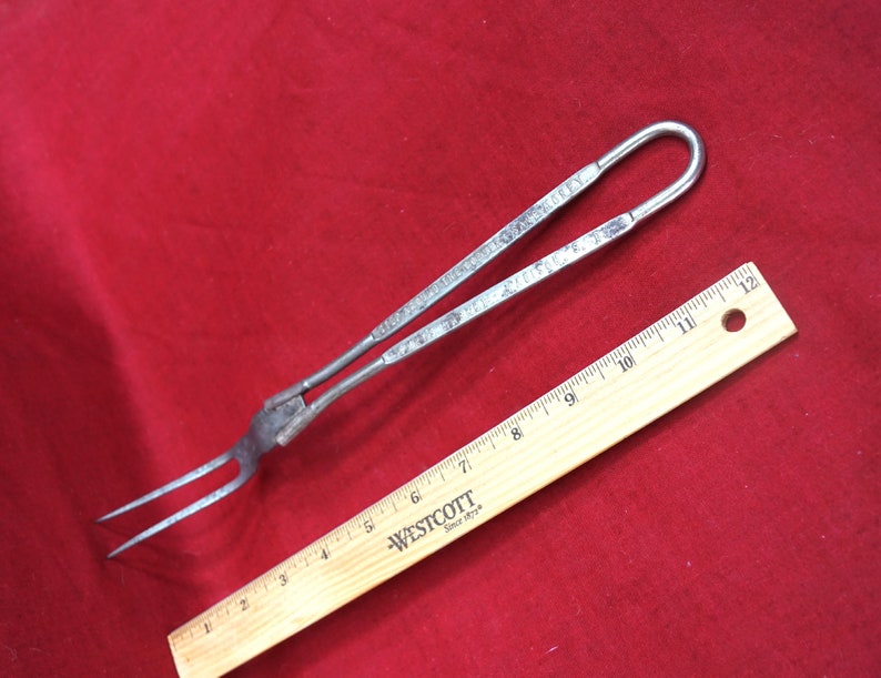 May include: A silver metal fork with a long handle and two prongs. The handle has a loop at the end and is marked with the text "PAT. JULY 17, 1906".