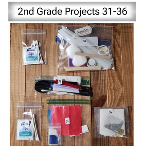 Może przedstawiać: Widok z g&oacute;ry na sześć przezroczystych plastikowych toreb z materiałami do majsterkowania dla projekt&oacute;w dla 2 klasy. Torby są oznaczone numerami 31-36 i zawierają takie przedmioty jak waciki, patyczki do lod&oacute;w i chusteczki. U g&oacute;ry znajduje się tekst "2nd Grade Projects 31-36".