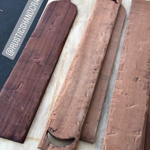 Op de afbeelding: Vijf 1,52 meter lange houten charcuterieplanken, drie zijn van natuurlijke houtkleur en twee zijn donkerbruin gebeitst. De planken zijn op elkaar gestapeld. De tekst "#CHARCUTERIEBOARD" staat in de rechterbovenhoek van de afbeelding. De tekst "@RUSTICSHANDCRAFTEDCO" staat in de linkerbovenhoek van de afbeelding. De tekst "CUSTOM REQUEST FOR A FRIEND" staat in de linkerbenedenhoek van de afbeelding. De tekst "5' CHARCUTERIE BOARDS" staat in het midden onderaan de afbeelding. De tekst "🥰" staat in de rechterbenedenhoek van de afbeelding.