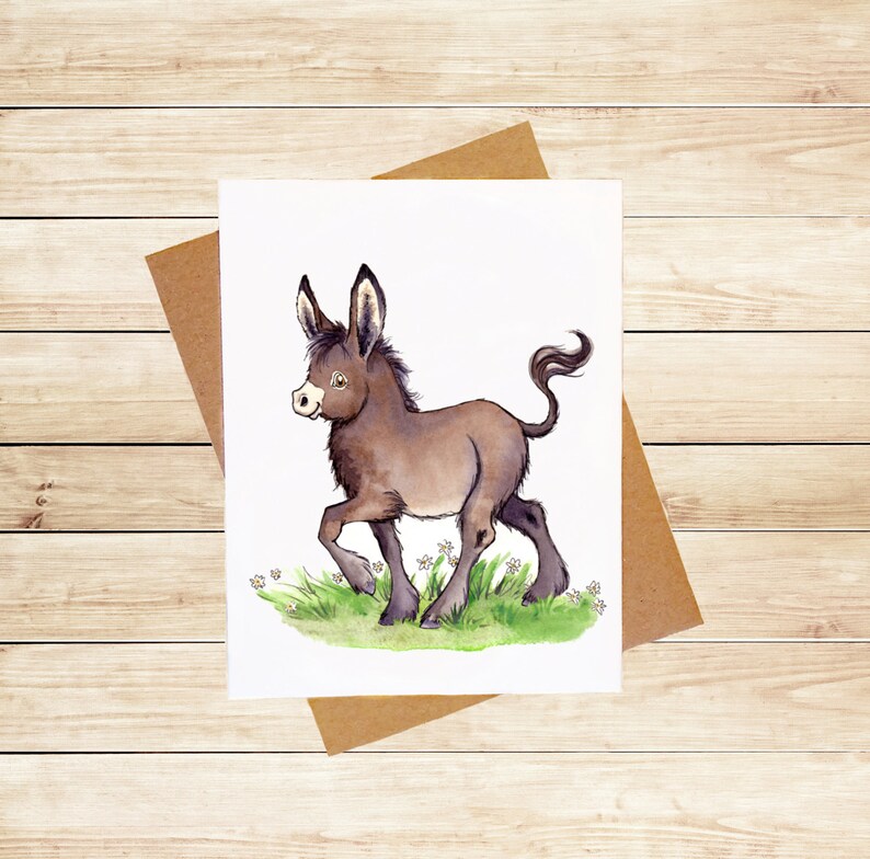 May include: A watercolor illustration of a brown donkey with a white face and a long tail. The donkey is standing in a field of green grass with white flowers.