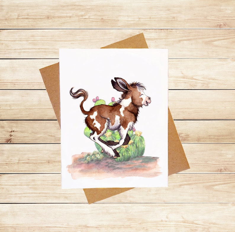 May include: A watercolor painting of a brown and white spotted donkey running through a field of green cactus plants.