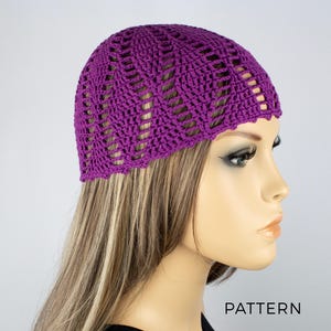 Könnte beinhalten: Lilafarbene Häkelmütze mit einem Spitzenmuster. Die Mütze wird von einer Mannequin mit langen braunen Haaren getragen.