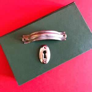 Peut inclure: Une poignée de porte en métal argenté avec un trou de serrure découpé. La poignée est sur une couverture de livre verte.