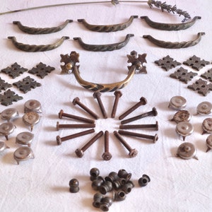May include: A collection of antique brass cabinet hardware, including drawer pulls, hinges, and screws. The hardware is arranged on a white surface.
