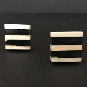 Peut inclure: Deux poignées de tiroir décoratives de forme carrée avec un motif rayé noir et blanc.