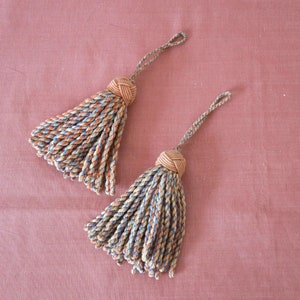 May include: Two decorative tassels with a brown and blue twisted cord design. The tassels are made of a soft, woven material and have a brown knot at the top.