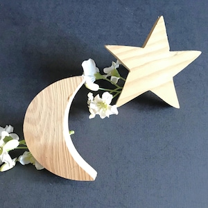 May include: Wooden crescent moon and star shapes, both painted in a light wood tone. The moon is slightly curved and the star has five points. The shapes are arranged so that the star is partially overlapping the moon.