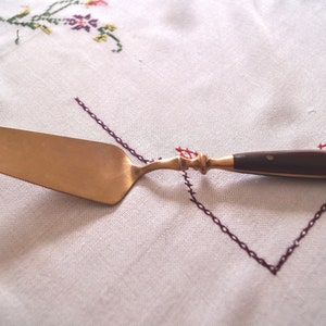 Peut inclure: Un serveur à gâteau doré avec un manche en bois. Le serveur a une lame large et plate et un manche légèrement incurvé.