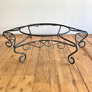 May include: A black metal plant stand with a round top and decorative scrollwork. The stand has three legs and features small floral accents.