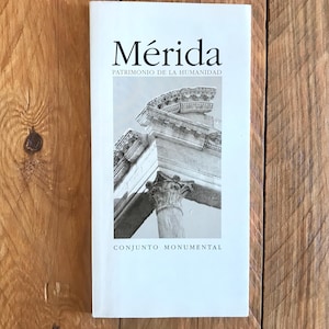 以下が含まれることがあります： 「メリダ」というタイトルと「Patrimonio de la Humanidad」と「Conjunto Monumental」というテキストが書かれた白い本。表紙には石のアーチの白黒写真が掲載されている。