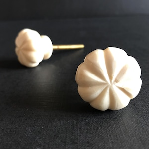 May include: Two white ceramic cabinet knobs with a fluted design and gold screws.