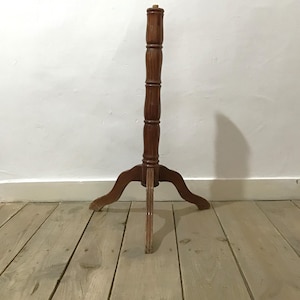 Può includere: Un espositore in legno marrone caratterizzato da un alto montante centrale cilindrico con scanalature orizzontali decorative e una base a tre gambe. Il supporto è realizzato con una finitura liscia e lucida e una solida struttura a treppiede.