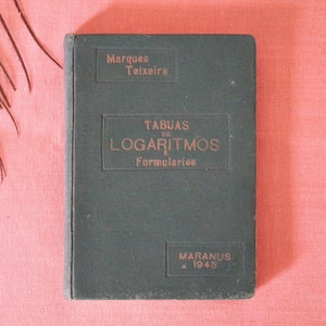 Puede incluir: Un libro de tapa dura de color verde oscuro titulado "Tabuas de Logaritmos e Formularios" de Marques Teixeira. El libro fue publicado en 1945 por Maranus.
