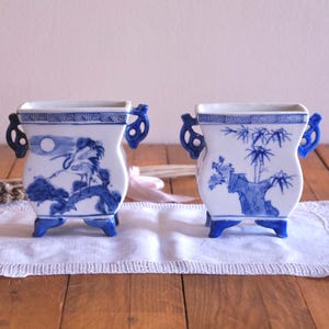 May include: Two blue and white porcelain planters with decorative designs. The planter on the left features a bird and moon, while the planter on the right features bamboo.