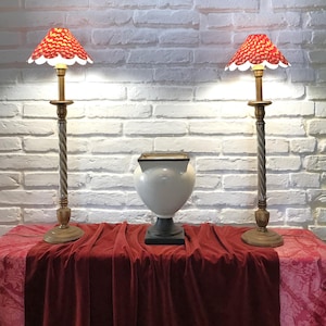 Könnte beinhalten: Zwei dekorative Tischlampen mit rot-weiß gemusterten Schirmen flankieren eine weiße Vase auf einem rot drapierten Tisch. Die Lampen haben gold- und silberfarbene, gedrehte Metallstiele.