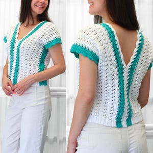 May include: A short-sleeved crochet top featuring a white openwork pattern with vertical teal stripes. The garment has a V-neckline on the front and a deep V-shaped back, with teal trim on the sleeves and along the central vertical panels.