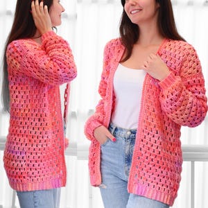 May include: A vibrant, open-front crochet cardigan in shades of pink and orange. The long-sleeved sweater features a loose, open weave design. The cardigan is a knee-length style, perfect for layering.