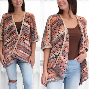 Puede incluir: Un cárdigan de crochet hecho a mano, abierto por delante, en una mezcla de colores melocotón, gris y crema. La prenda de manga corta presenta un patrón geométrico y un ribete de color neutro. El cárdigan se lleva sobre un top marrón y unos vaqueros azules.