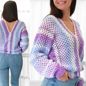 May include: A crocheted sweater with a V-neck and long sleeves. The sweater is made with a light purple, blue, and white yarn and has a striped pattern.