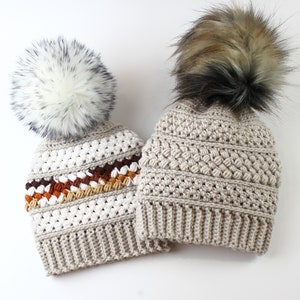 May include: Two crocheted hats with faux fur pom poms. One hat is beige with a white stripe and a brown, orange, and beige stripe. The other hat is beige.