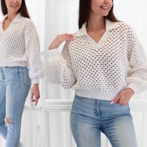 May include: White crochet sweater with a v-neck and a collared neckline. The sweater has a loose fit and a textured design.