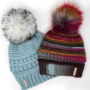 May include: Two crocheted hats with faux fur pom poms. One hat is light blue with a white pom pom and the other is multi-colored with a red, brown, and gray pom pom.