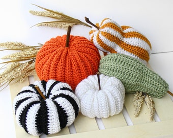 May include: Five crocheted pumpkins in various colours and patterns. The pumpkins are arranged on a wooden surface. The pumpkins are orange, white, green, black, and yellow.