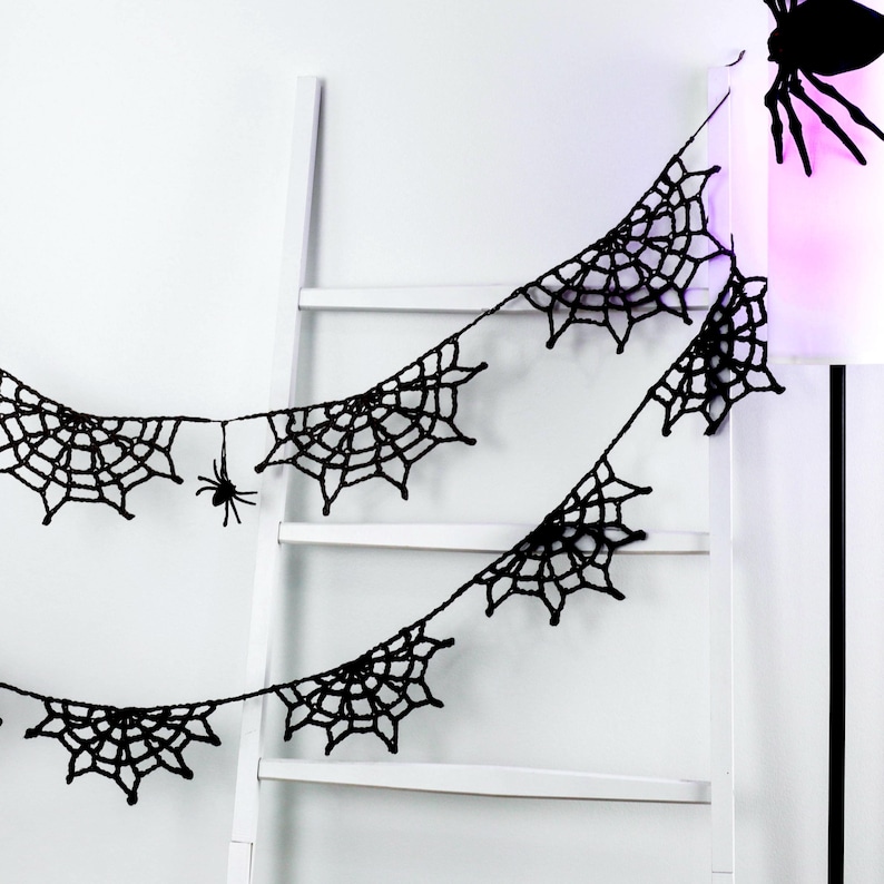 May include: A black crocheted garland featuring multiple interconnected spider web motifs and a small dangling spider. The decorative string is crafted from dark yarn and displays a repeating pattern of web segments linked together.