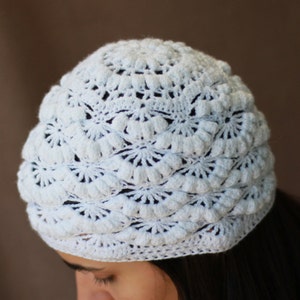 Op de afbeelding: Witte gebreide beanie met een textuurrijk, kantpatroon. De beanie is gemaakt met een delicaat steekpatroon dat een unieke en stijlvolle look creëert.