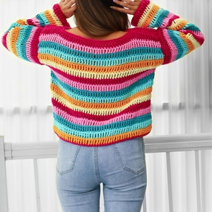 Peut inclure: Un pull en crochet ray&eacute; color&eacute; avec une coupe ample et des manches longues. Le pull est r&eacute;alis&eacute; avec une vari&eacute;t&eacute; de couleurs vives, dont le rose, l'orange, le jaune, le bleu et le vert.