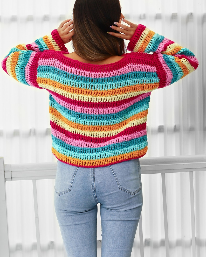 Peut inclure: Un pull en crochet ray&eacute; color&eacute; avec une coupe ample et des manches longues. Le pull est r&eacute;alis&eacute; avec une vari&eacute;t&eacute; de couleurs vives, dont le rose, l'orange, le jaune, le bleu et le vert.