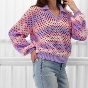 Peut inclure: Un pull en crochet avec un col en V et des manches longues. Le pull est r&eacute;alis&eacute; dans un motif ray&eacute; de fil rose, violet et blanc. Le pull est ample et a un style d&eacute;contract&eacute;.