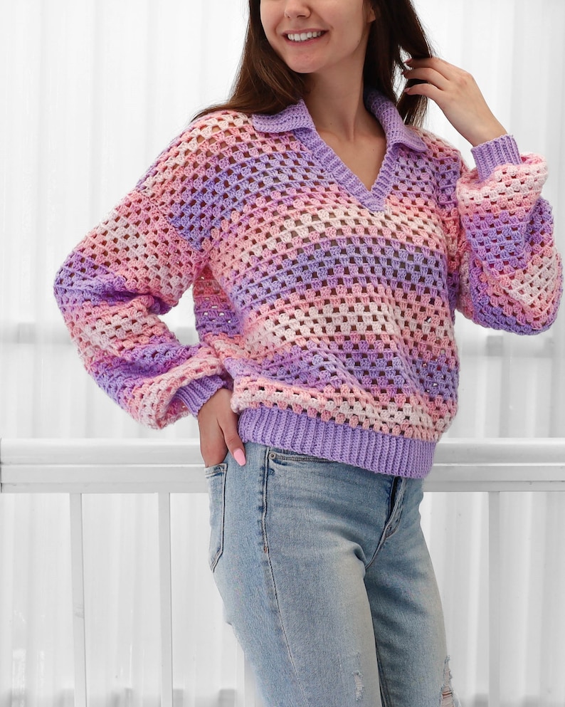 Peut inclure: Un pull en crochet avec un col en V et des manches longues. Le pull est r&eacute;alis&eacute; dans un motif ray&eacute; de fil rose, violet et blanc. Le pull est ample et a un style d&eacute;contract&eacute;.