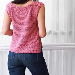 May include: A pink crochet top with a scoop neck and short sleeves. The top is made with a simple stitch pattern and has a delicate crocheted trim around the neckline.