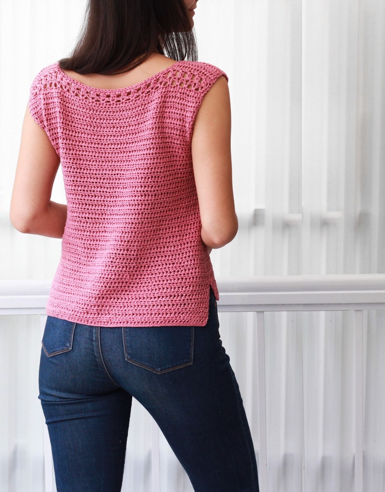 May include: A pink crochet top with a scoop neck and short sleeves. The top is made with a simple stitch pattern and has a delicate crocheted trim around the neckline.