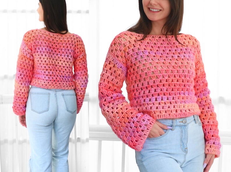 May include: A cropped, open-weave crochet sweater in shades of pink, orange, and purple. The sweater has long sleeves and a boat neck. The model is wearing light blue jeans. The sweater's texture and color gradient are prominent.