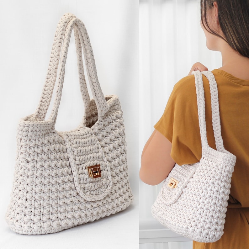 Puede incluir: Un bolso tote blanco de crochet con un cierre dorado. El bolso tiene un dise&ntilde;o texturizado y tejido y se muestra sobre un fondo blanco.