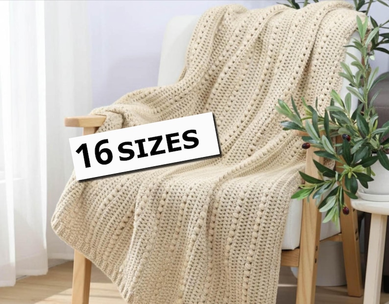 Pu&ograve; includere: Una coperta lavorata a maglia color crema drappeggiata su una sedia di legno. La coperta ha un motivo strutturato con piccoli fori distanziati. Il testo "16 SIZES" &egrave; visualizzato su un rettangolo bianco. Una pianta in vaso &egrave; visibile sullo sfondo.