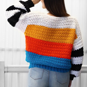 May include: A colorful striped crochet sweater with black and white stripes on the sleeves. The sweater is made with a variety of colors, including white, yellow, orange, red, and blue.