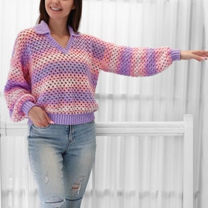 Peut inclure: Un pull en crochet ray&eacute; violet, rose et blanc avec un col en V et un col. Le pull est ample et r&eacute;alis&eacute; avec un fil l&eacute;ger.