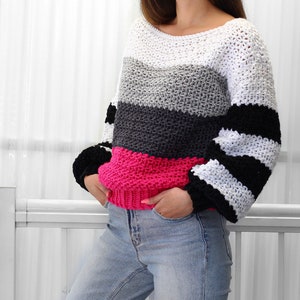 May include: A striped crochet sweater with a white, gray, black, and pink color scheme. The sweater has a boat neck and long sleeves.
