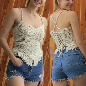 Puede incluir: Un top blanco de crochet con un dobladillo con flecos y un dise&ntilde;o de espalda cruzada. El top se lleva con pantalones cortos de mezclilla.