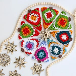 Puede incluir: Una colecci&oacute;n de adornos de &aacute;rbol de Navidad hechos a crochet en varios colores y patrones, incluyendo rojo, verde, azul y blanco. Los adornos est&aacute;n dispuestos en un c&iacute;rculo alrededor de una guirnalda de cuentas de madera.