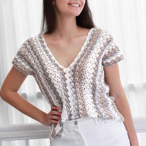 May include: A crocheted top with a V-neck and short sleeves. The top is made with a white, gray, and brown yarn and has a striped pattern.